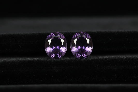 Perfectly matched purple amethyst gemstone pair on black velvet - identical 2.5ct oval cut stones with same deep royal purple color and eye-clean clarity demonstrating why matched pairs cost 3X more and take 6 months to find